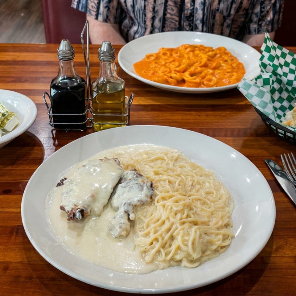 Restaurant table with creamy spaghetti and chicken, tomato-sauced pasta, bread basket, condiments, and iced water.