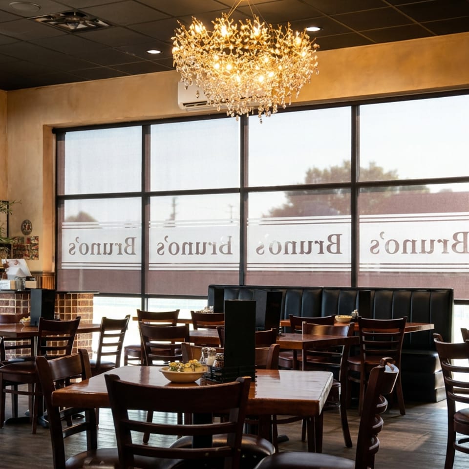 Bright restaurant dining room with wooden tables, leather booths, large windows, and an ornate chandelier.